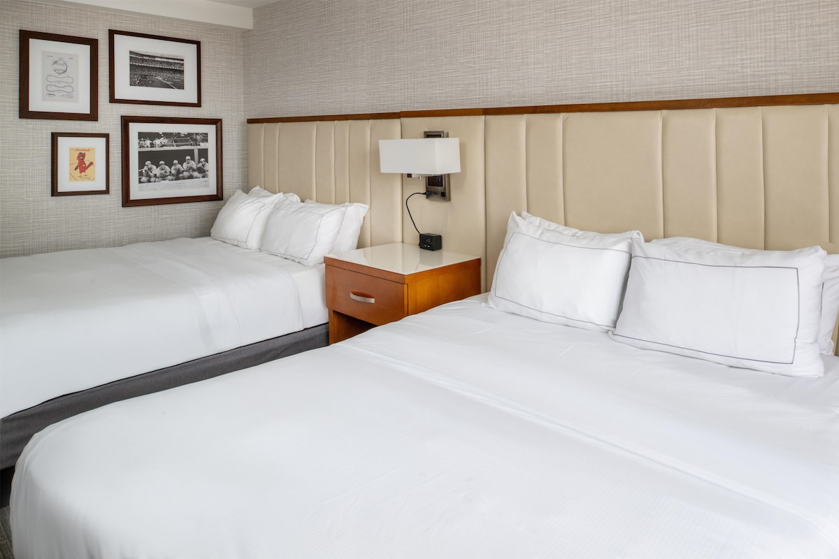 A hotel room with two beds, a nightstand, and a wall-mounted lamp.