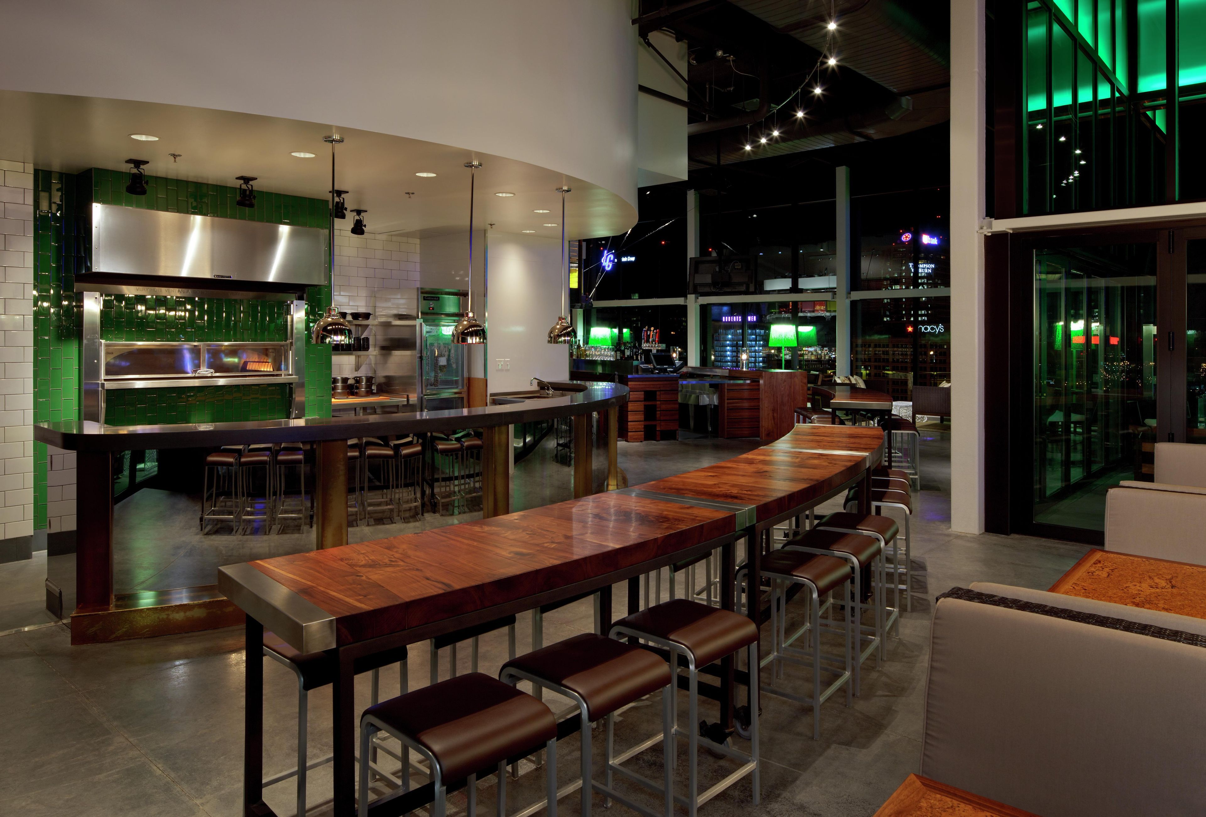 A modern bar area with a long counter, stools, and a kitchen in the background.