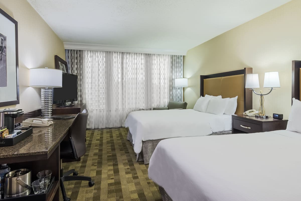 Habitación de hotel con dos camas, un escritorio, teléfono, lámpara y televisor.