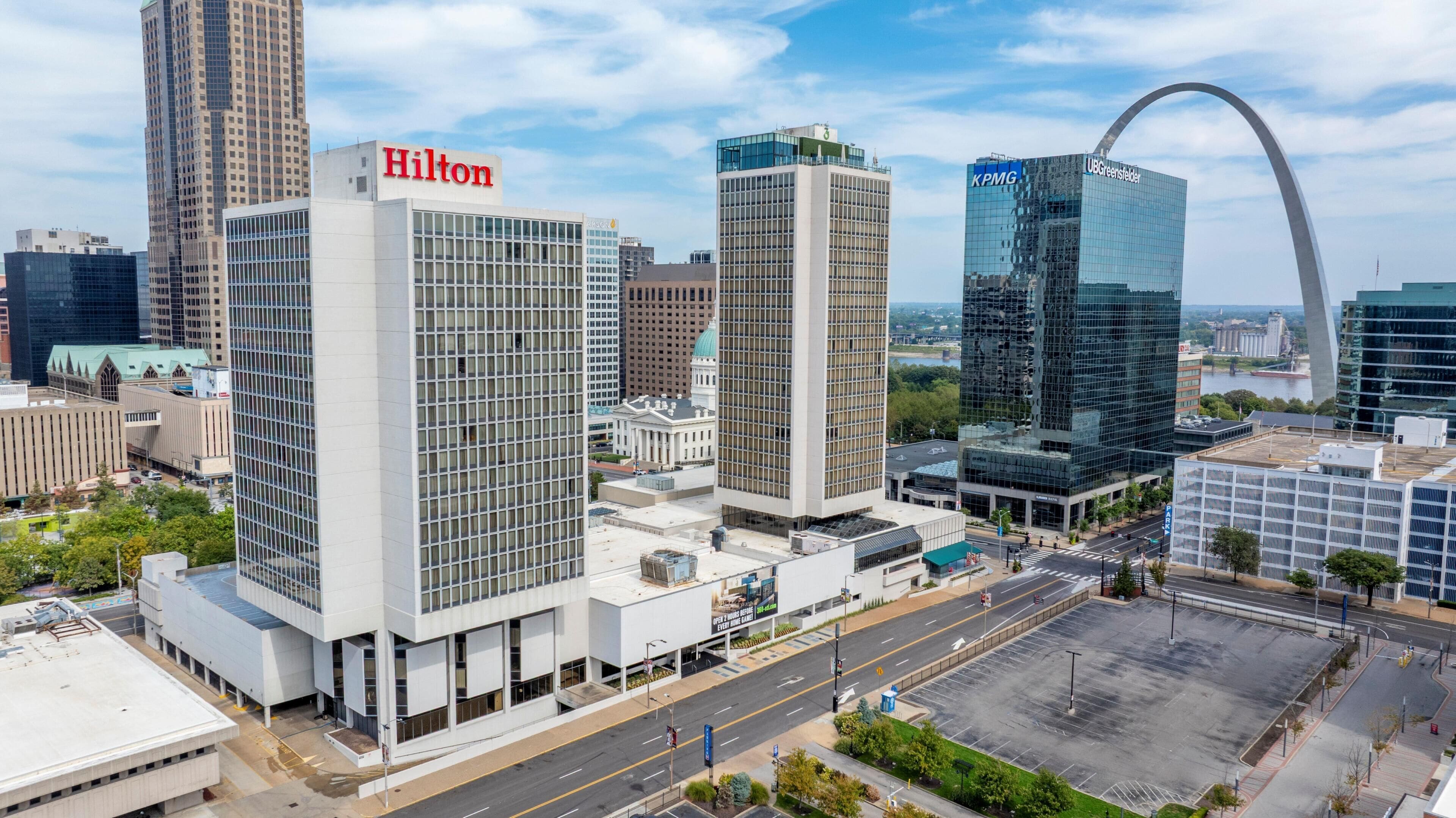 A modern hotel with a prominent Hilton sign, surrounded by high-rise buildings and a clear sky.