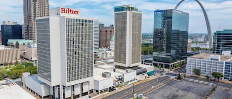 A modern hotel with a prominent Hilton sign, surrounded by high-rise buildings and a clear sky.