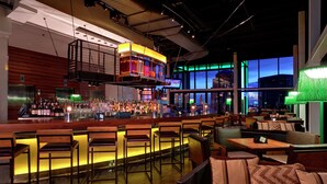 Un espace bar doté de tabourets en bois, d’un comptoir haut et d’un coin salon avec des canapés confortables et des tables.