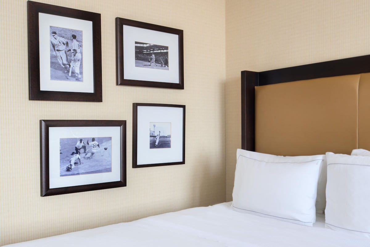 A hotel room with a bed, white pillows, and four framed black-and-white photographs on the wall.