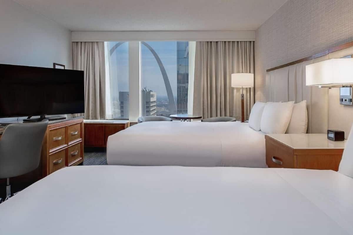 Habitación de hotel con una cama grande, televisión, escritorio, lámpara y vista a un puente.