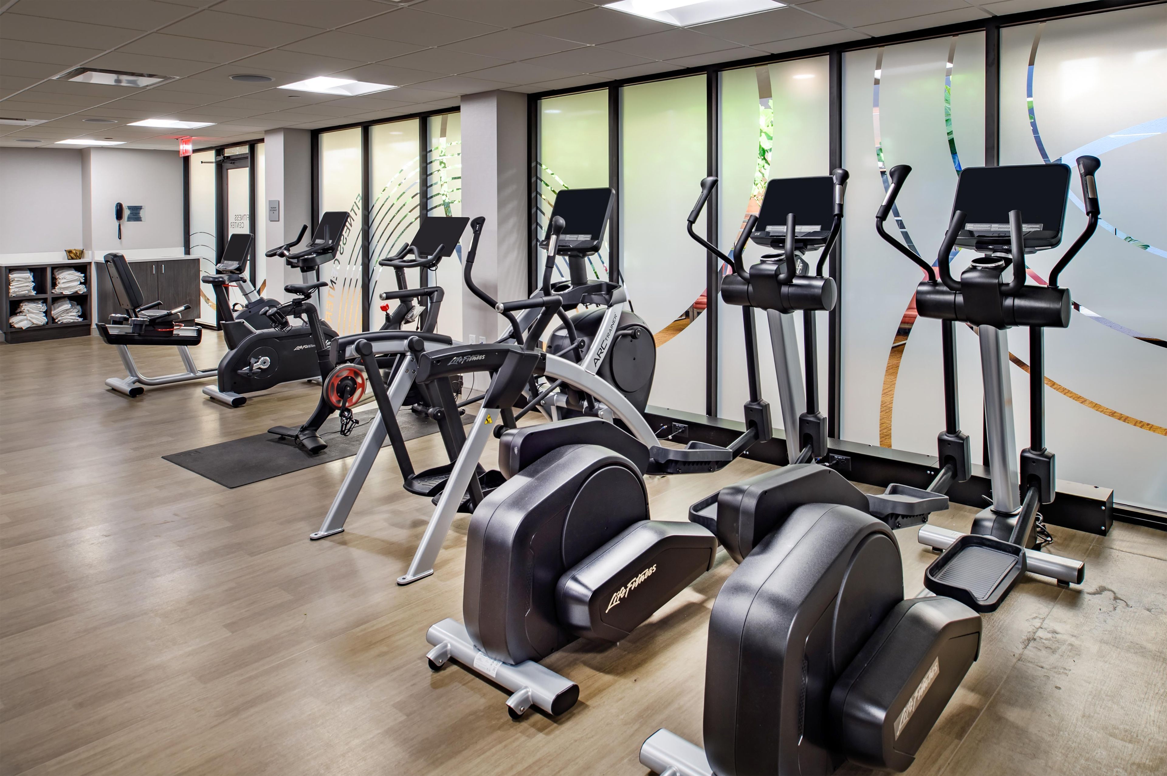 A gym with various exercise machines, including treadmills and stationary bikes, arranged in rows.