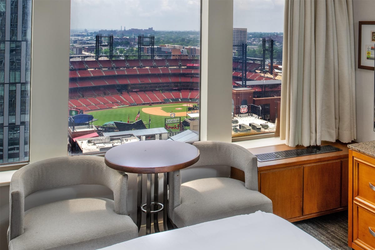 Habitación de hotel con un ventanal grande que ofrece vistas a un estadio de béisbol.
