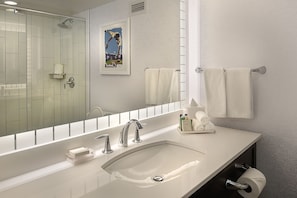 A modern bathroom with a large mirror, two sinks, a shower, and a towel rack. - Hilton St. Louis at the Ballpark (St. Louis)