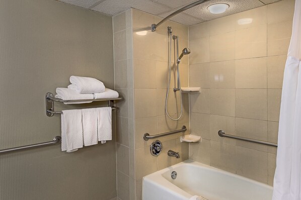Un baño moderno con una bañera, ducha con cabezal de ducha manual y un toallero con toallas dobladas.