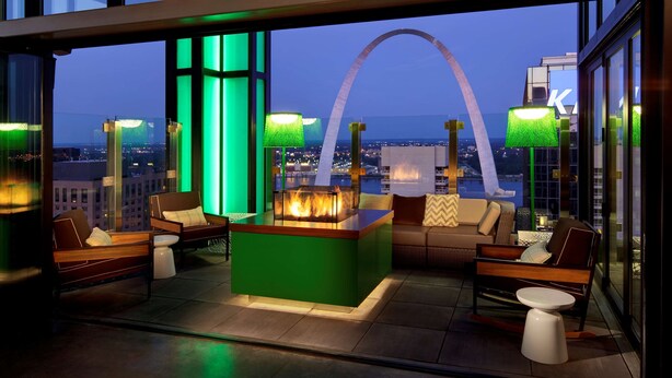 Un salon moderne doté d’un foyer central, de sièges confortables et de grandes fenêtres offrant une vue sur la ville.