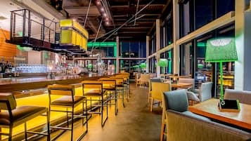 A bar area with seating and a bar counter, large windows, and a high ceiling with exposed beams.