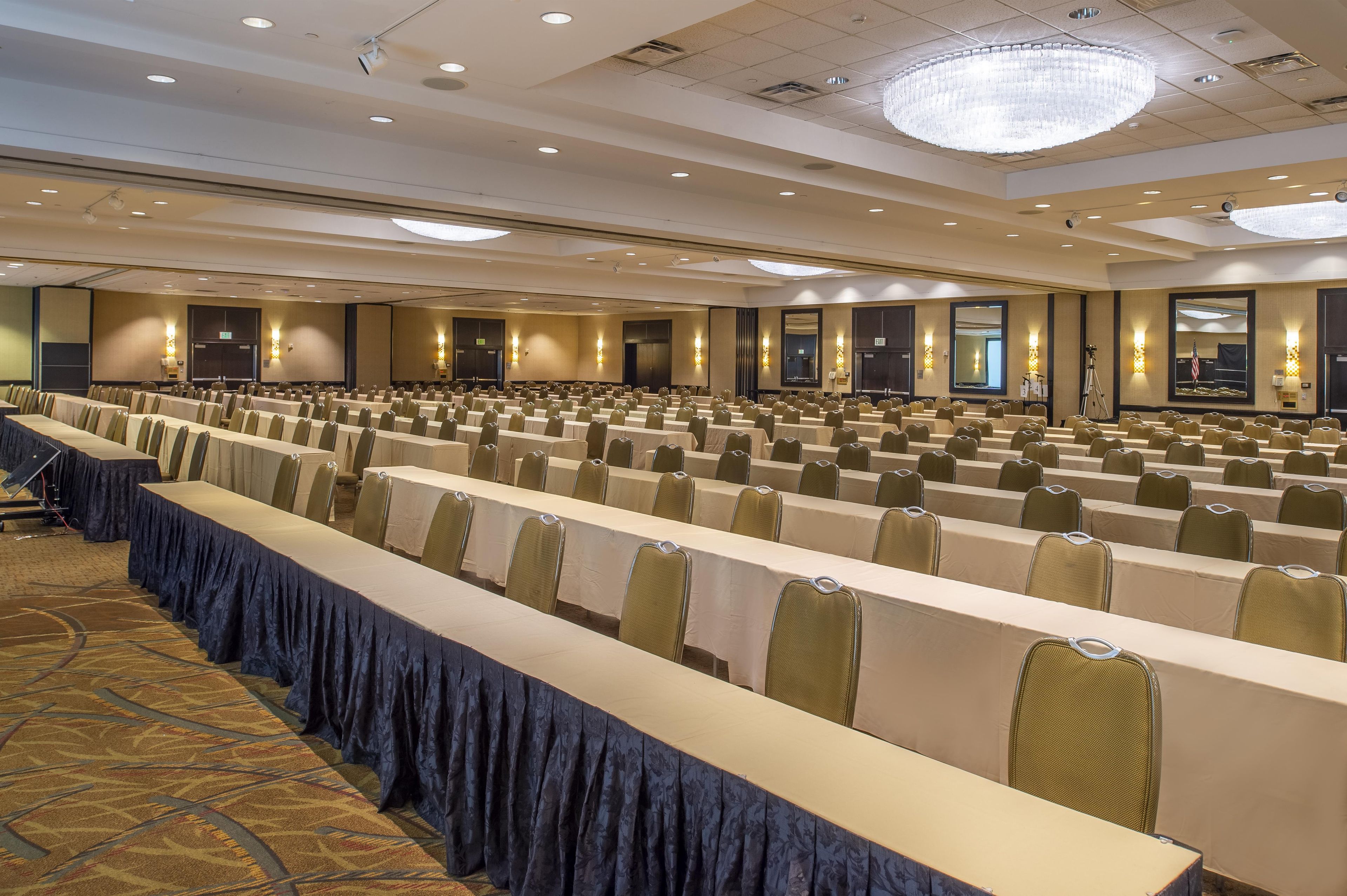 A conference room with rows of tables and chairs, a chandelier, and a large mirror on the wall.