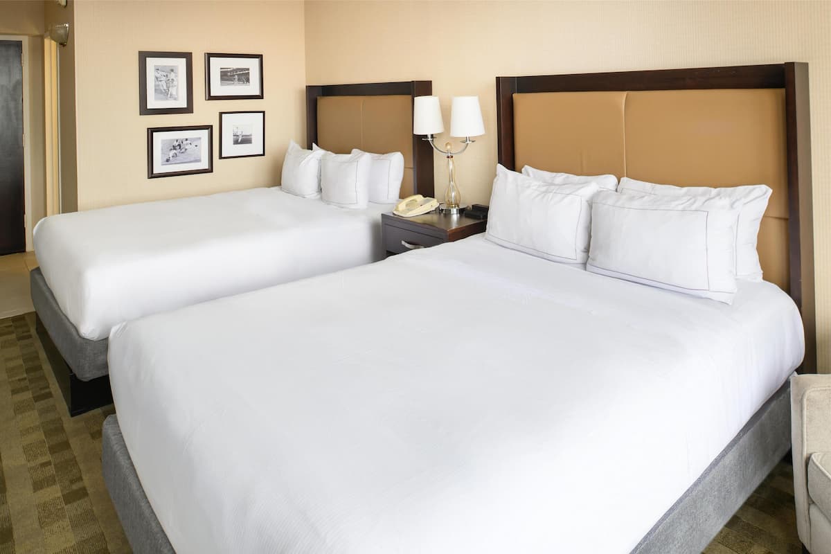 Habitación de hotel con dos camas, una mesita de noche con lámpara y cuadros en la pared.