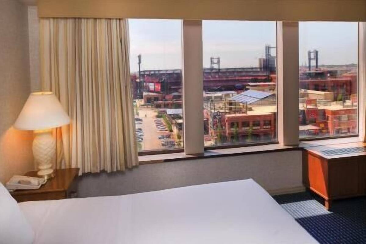 Una habitación de hotel con un ventanal grande, una cama, una lámpara y un escritorio.