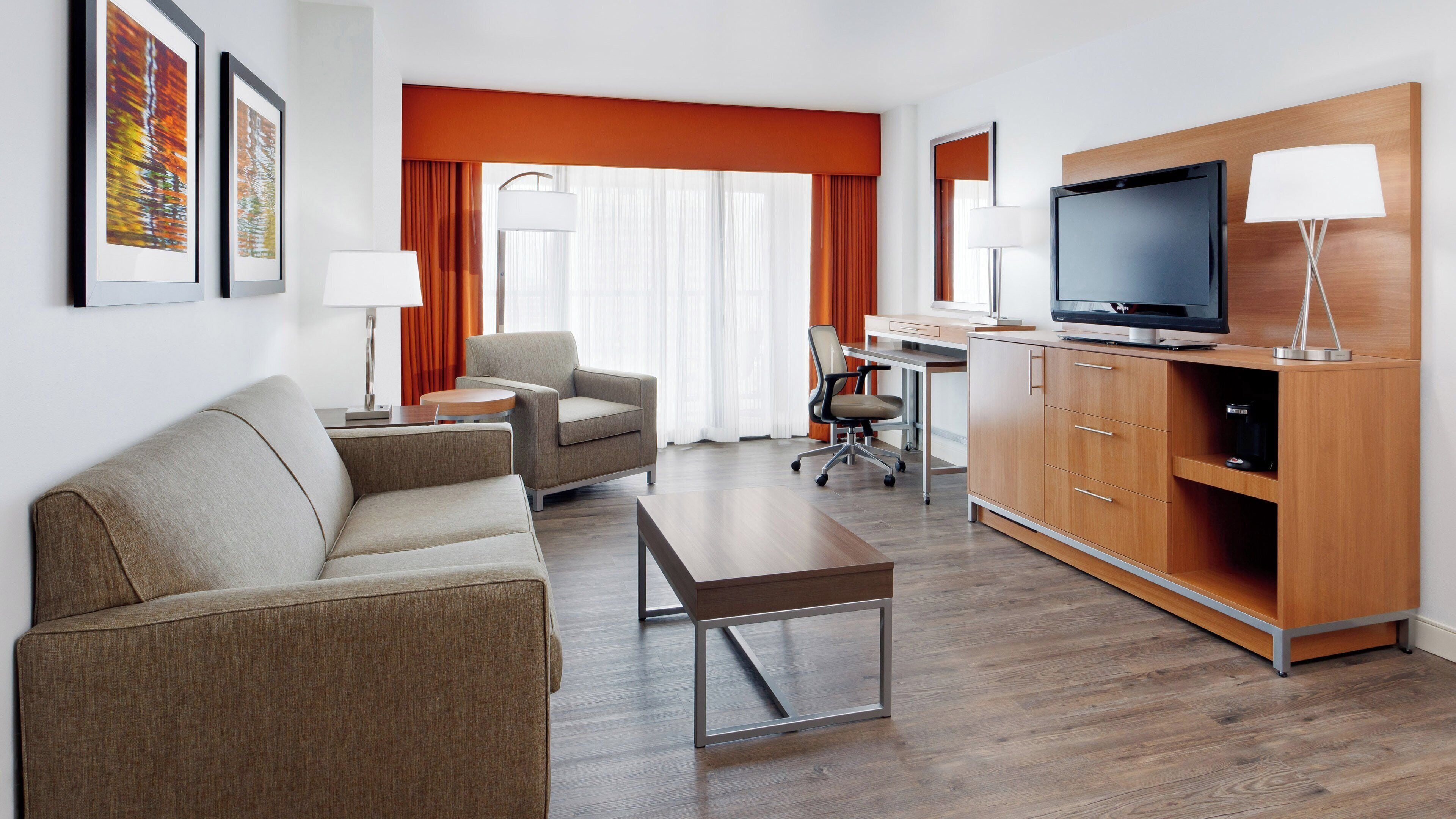 A hotel room with a sofa, armchair, TV, and wooden cabinet.
