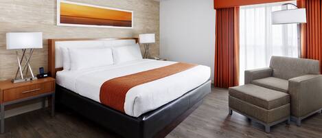 A hotel room with a large bed, a nightstand, a chair, and a window with curtains.
