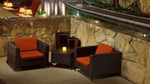 A stone wall seating area with wicker chairs and a small table, overlooking a water feature.
