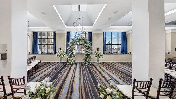 A spacious hall with a patterned carpet, rows of wooden chairs, and a central floral arrangement.