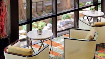 Habitación de hotel con un ventanal grande, una mesita redonda con un florero y dos sillones con cojines.