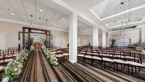 Un vestíbulo de hotel con un pasillo central que conduce a una zona de recepción, rodeado de filas de sillas de madera y un suelo alfombrado.