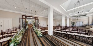 A hotel lobby with a central aisle leading to a reception area, surrounded by rows of wooden chairs and a carpeted floor. - Holiday Inn San Antonio - Riverwalk by IHG (San Antonio)