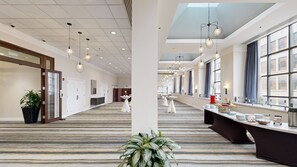 A hotel lobby with a long reception desk, multiple tables, and a large window with curtains. - Holiday Inn San Antonio - Riverwalk by IHG (San Antonio)