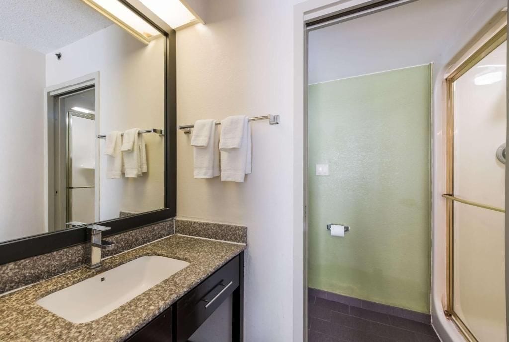 Un baño con lavamanos de encimera de granito, un espejo y un perchero con varias toallas.