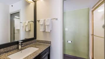 Un baño con lavamanos de encimera de granito, un espejo y un perchero con varias toallas.