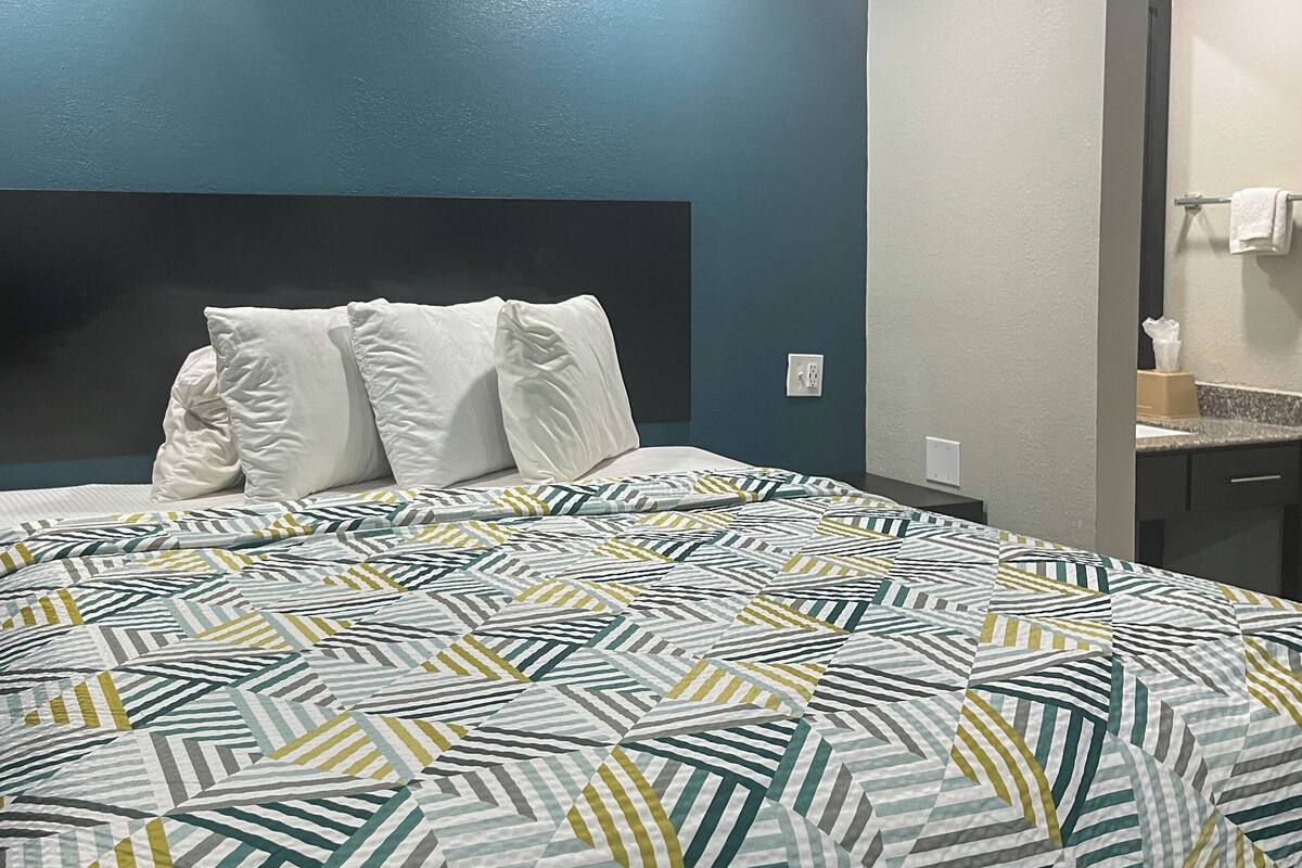 A hotel room with a bed, a nightstand, a mirror, and a towel rack.