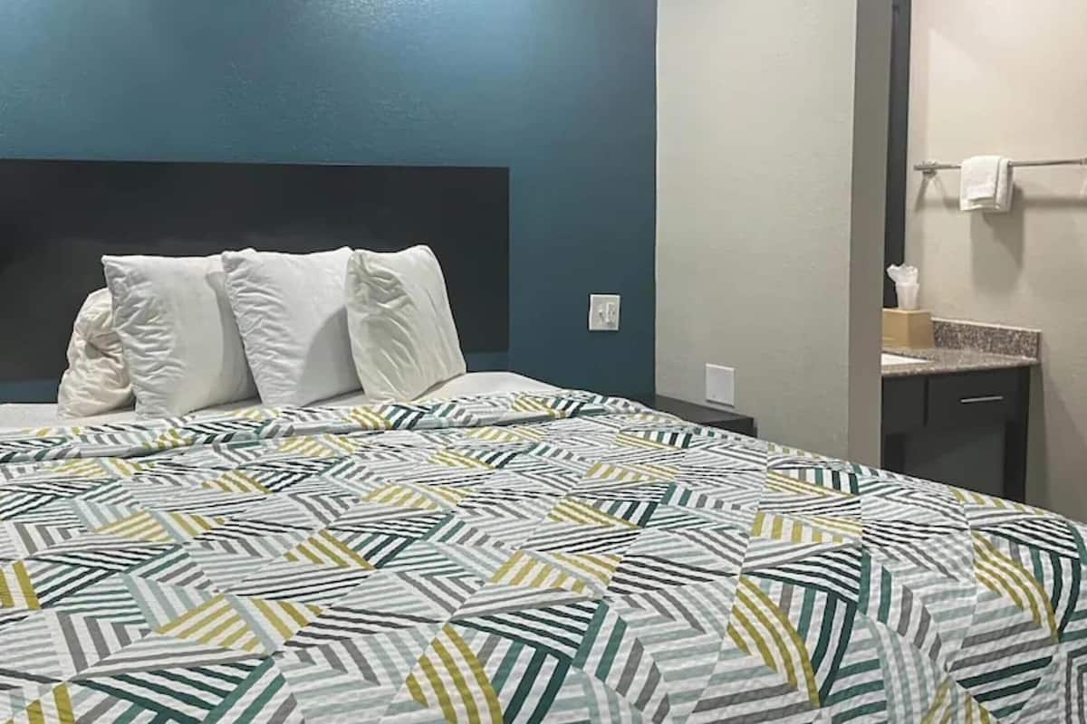 A hotel room with a bed, a headboard, a bathroom with a towel rack, and a counter.