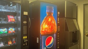 Un distributeur automatique orné d’une image d’une bouteille de Pepsi, qui accepte les pièces et les billets.