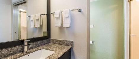 A bathroom with a granite countertop, a white sink, and a towel rack with white towels.