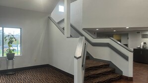 Un hall d’hôtel moderne avec un escalier, une plante en pot et une moquette à motifs.