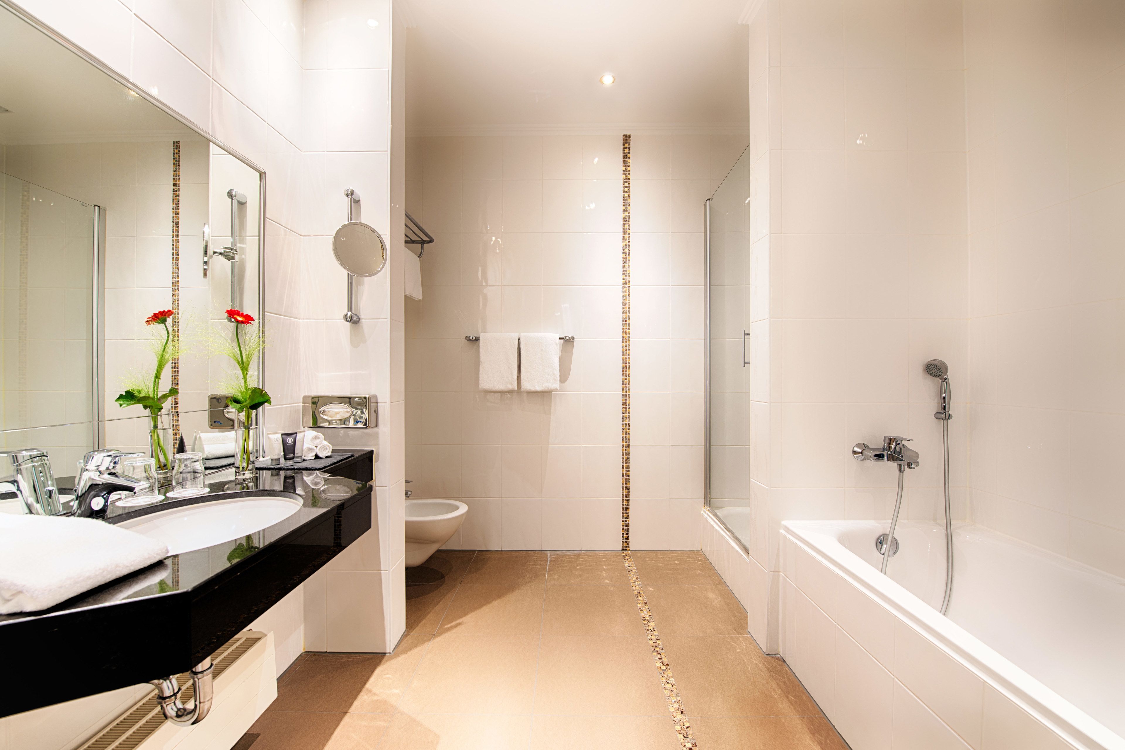 A modern bathroom with a large mirror, two sinks, a toilet, and a bathtub.