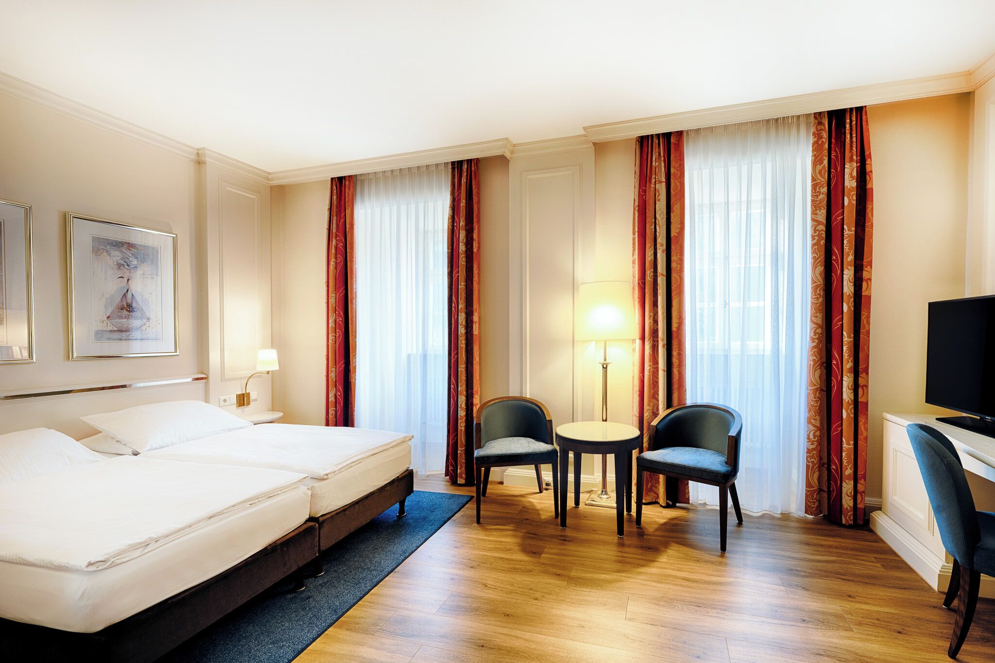 Habitación de hotel con dos camas, un escritorio, una silla y un televisor.