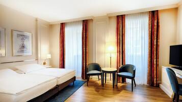 Habitación de hotel con dos camas, un escritorio, una silla y un televisor.