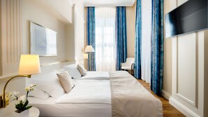 Een hotelkamer met een groot bed, een bureau met lamp, een stoel en een televisie aan de muur.