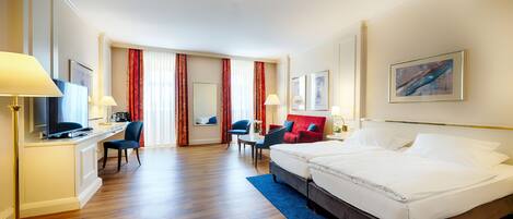 Una habitación de hotel con cama, dos sillas, escritorio, televisor y ventana con cortinas.