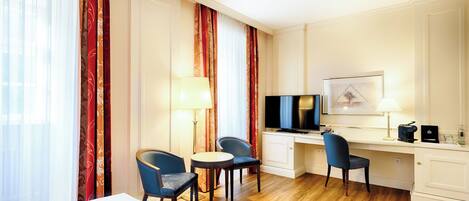 Habitación de hotel con cama, dos sillas, escritorio con computadora, televisión y lámpara.