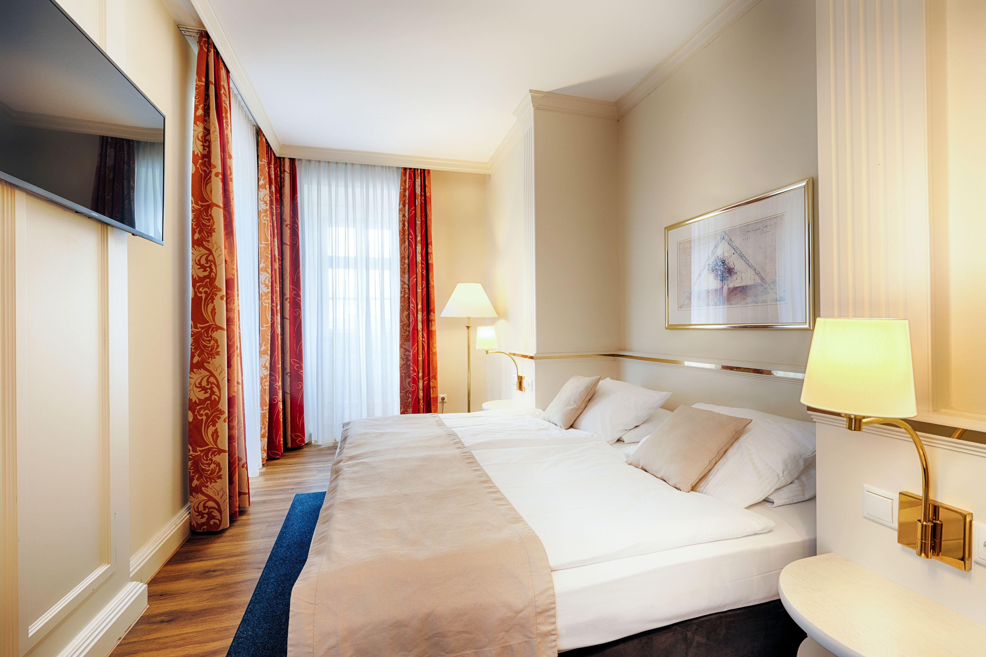 Een hotelkamer met een groot bed, een flatscreen televisie, een bureau met een lamp en een lijst aan de muur.