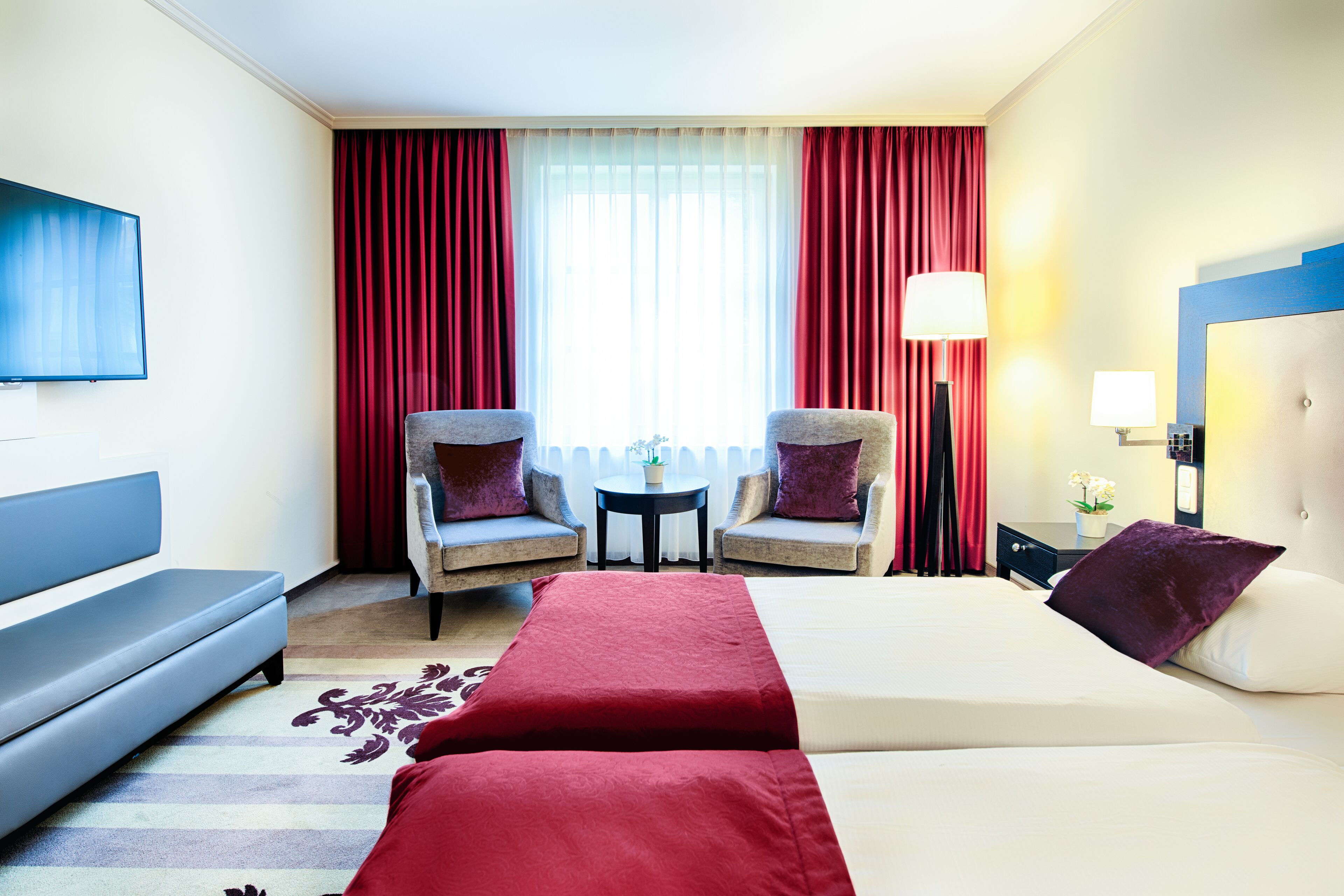 A hotel room with a bed, two armchairs, a sofa, a small table, and a TV.