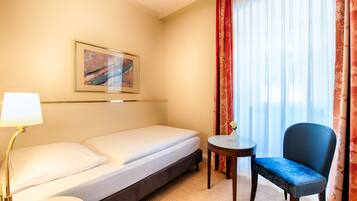A hotel room with a bed, a chair, a small table, a lamp, and a painting on the wall.