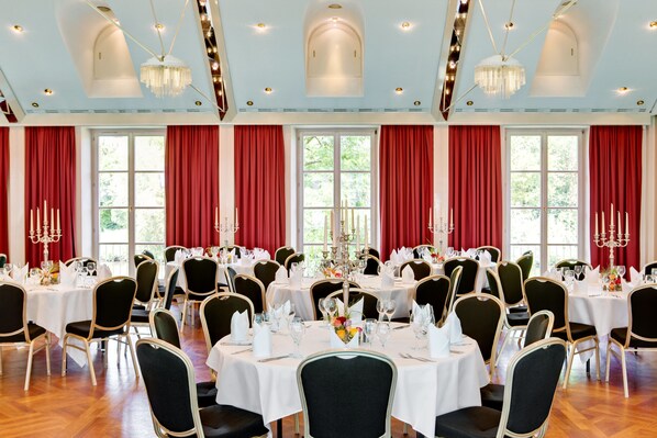 Un comedor formal con mesas redondas, sillas tapizadas en negro y cortinas rojas.