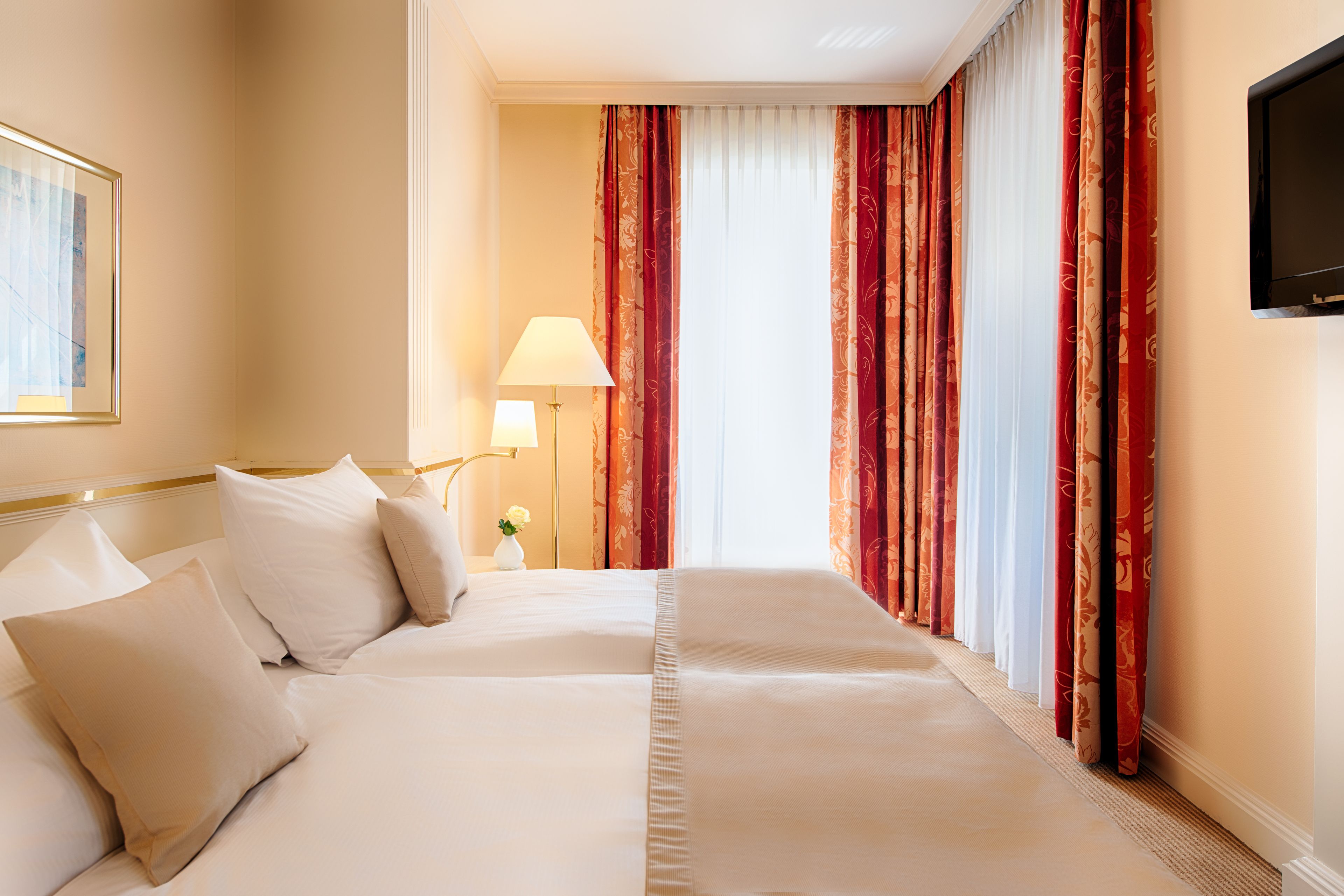 Een hotelkamer met een groot bed, een nachtkastje met een lamp en een televisie aan de muur.