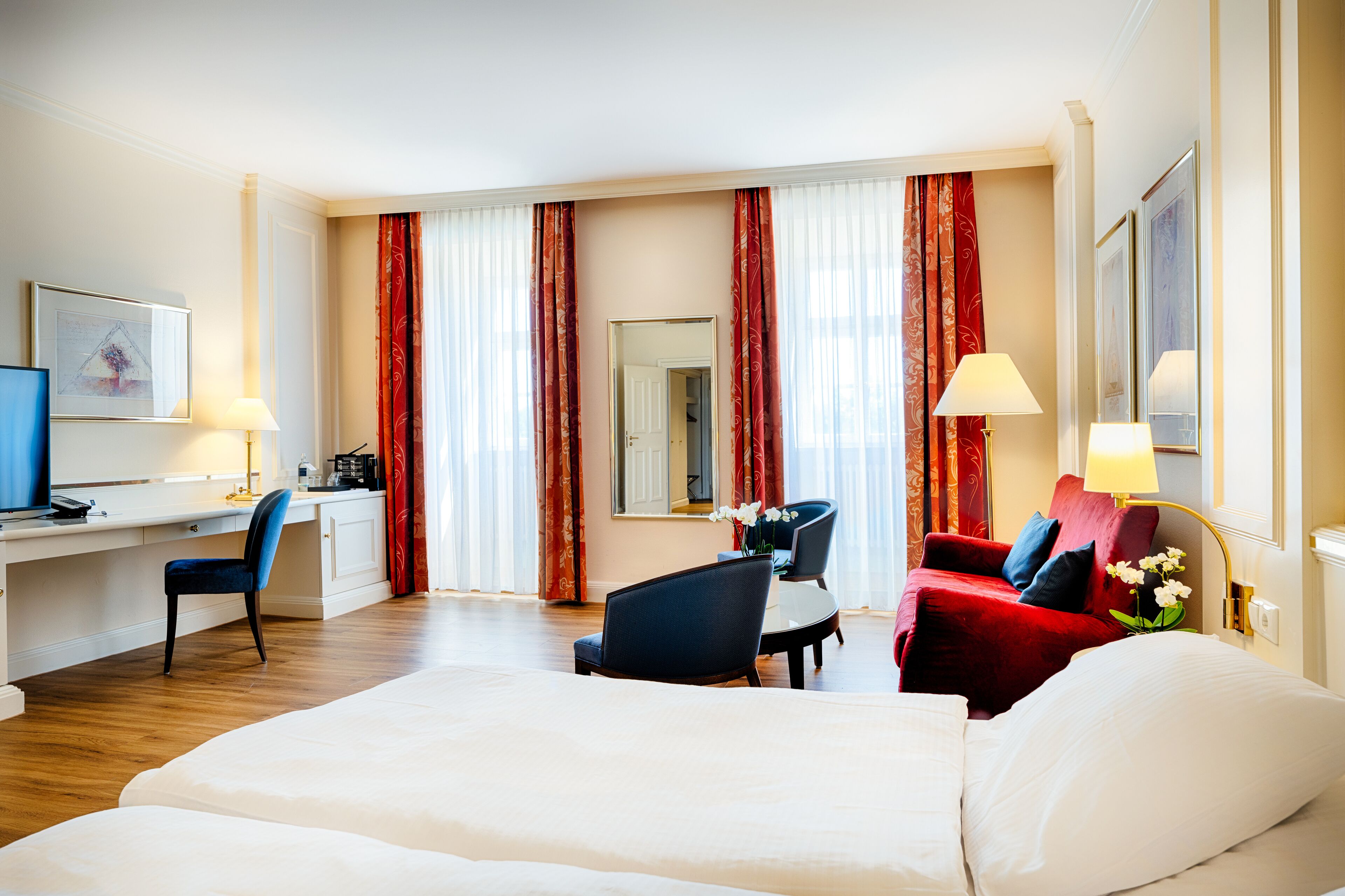 A hotel room with a bed, desk, chair, and a red sofa.