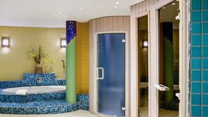 Een badkamer met een blauw betegeld bubbelbad, een glazen douchecabine en een houten bankje.