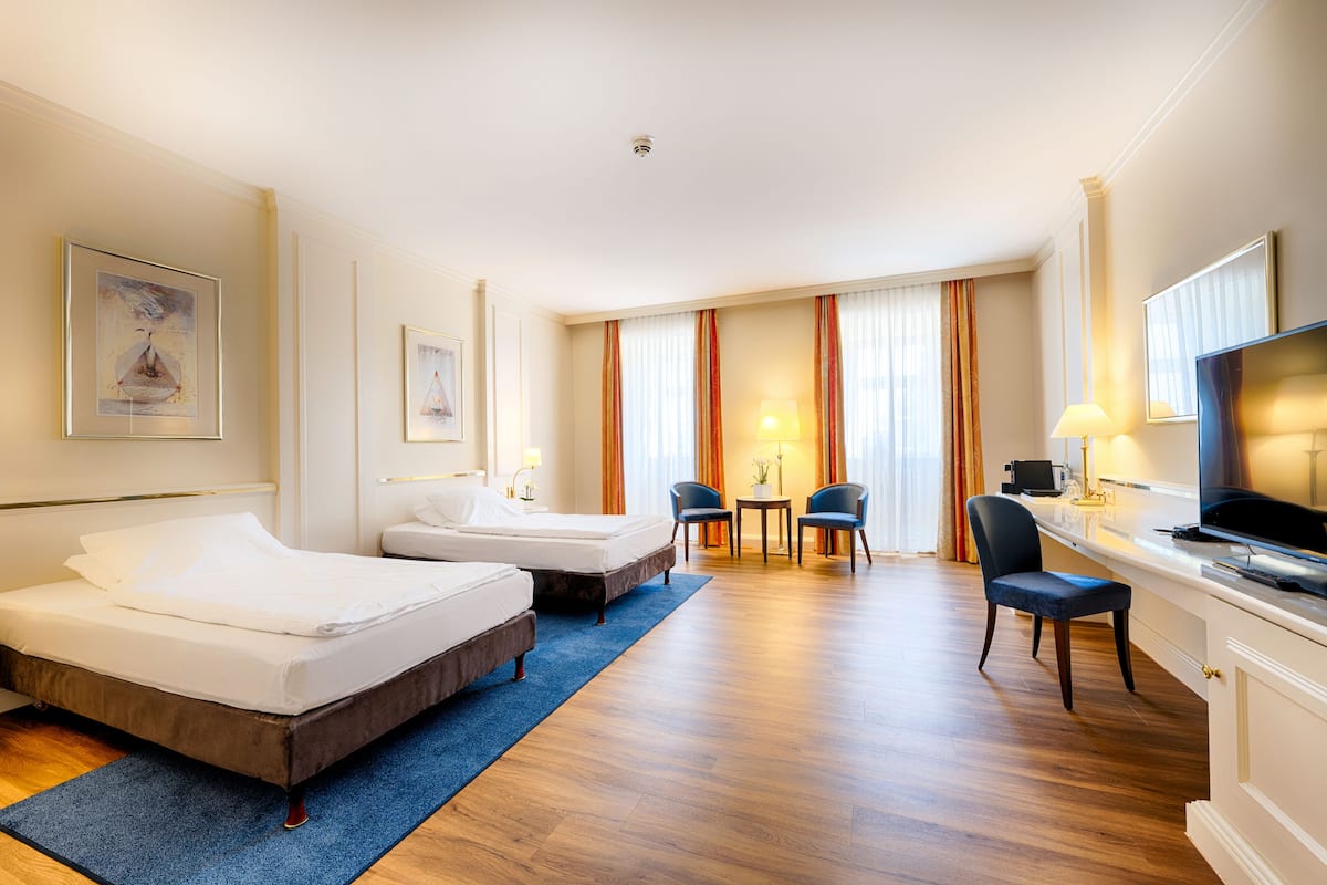 Ein Hotelzimmer mit zwei Betten, einem Schreibtisch mit Fernseher und einer Sitzecke mit Stühlen.