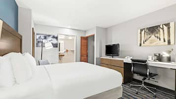 A hotel room with a bed, desk, chair, TV, and artwork.
