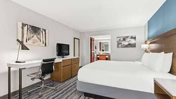 A hotel room with a large bed, a desk with a chair, a television, and a bathroom visible through an open door.