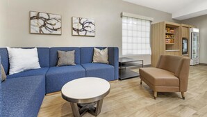 A modern living room with a blue sectional sofa, a round coffee table, a tan armchair, and abstract art on the walls.