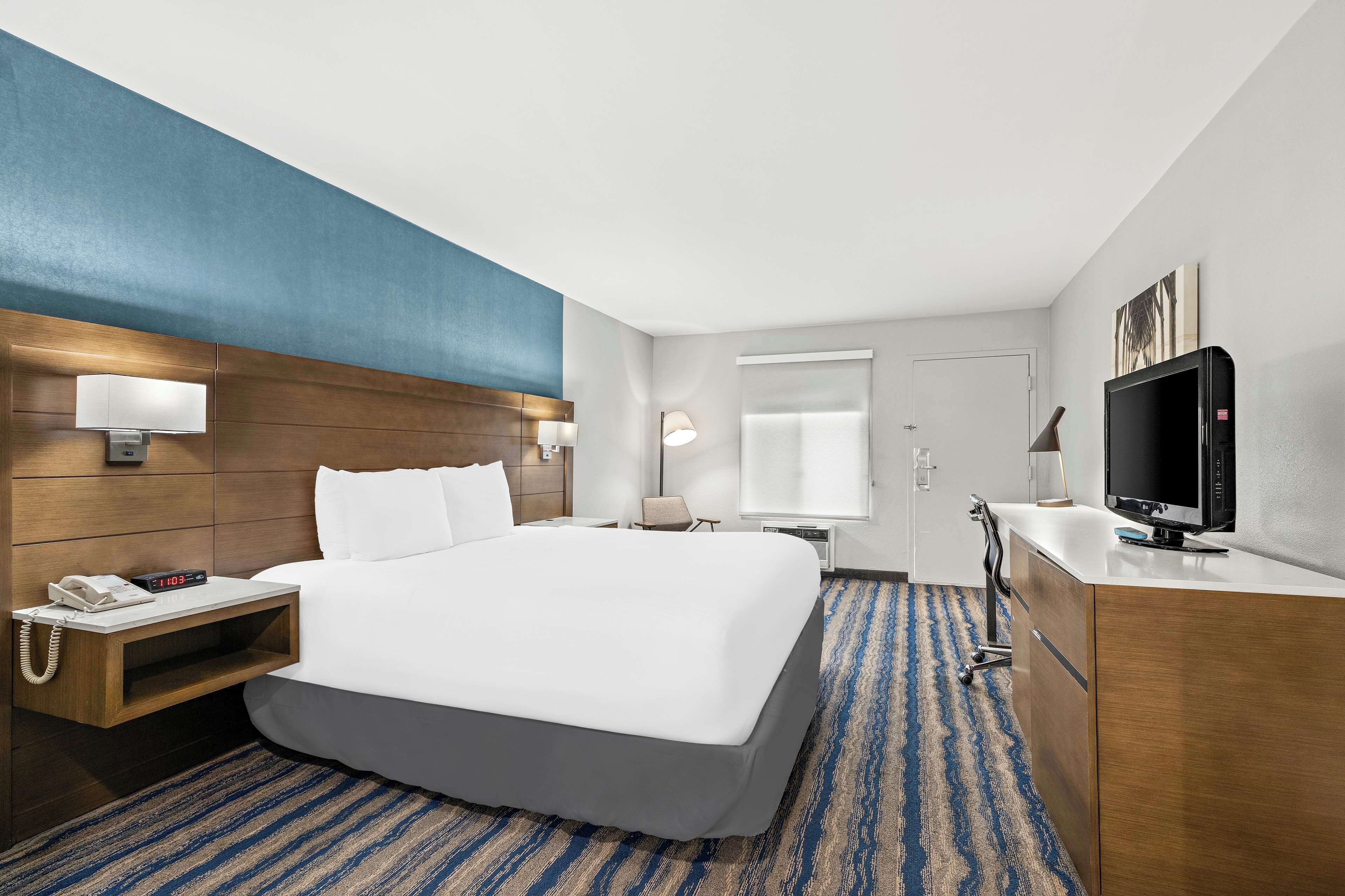 A hotel room with a large bed, a desk with a computer, a TV, and a telephone on the nightstand.